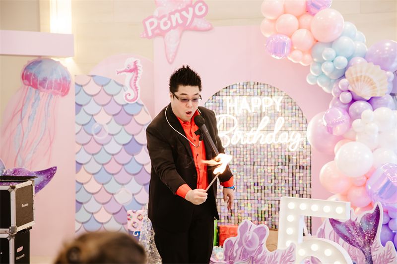 Magician performing in front of a mermaid birthday backdrop